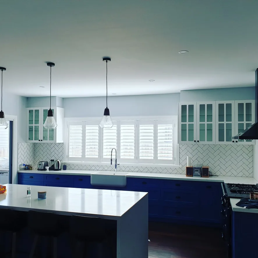 Custom plantation shutters in a styled Melbourne kitchen with blue cabinetry — We Inspire Blinds