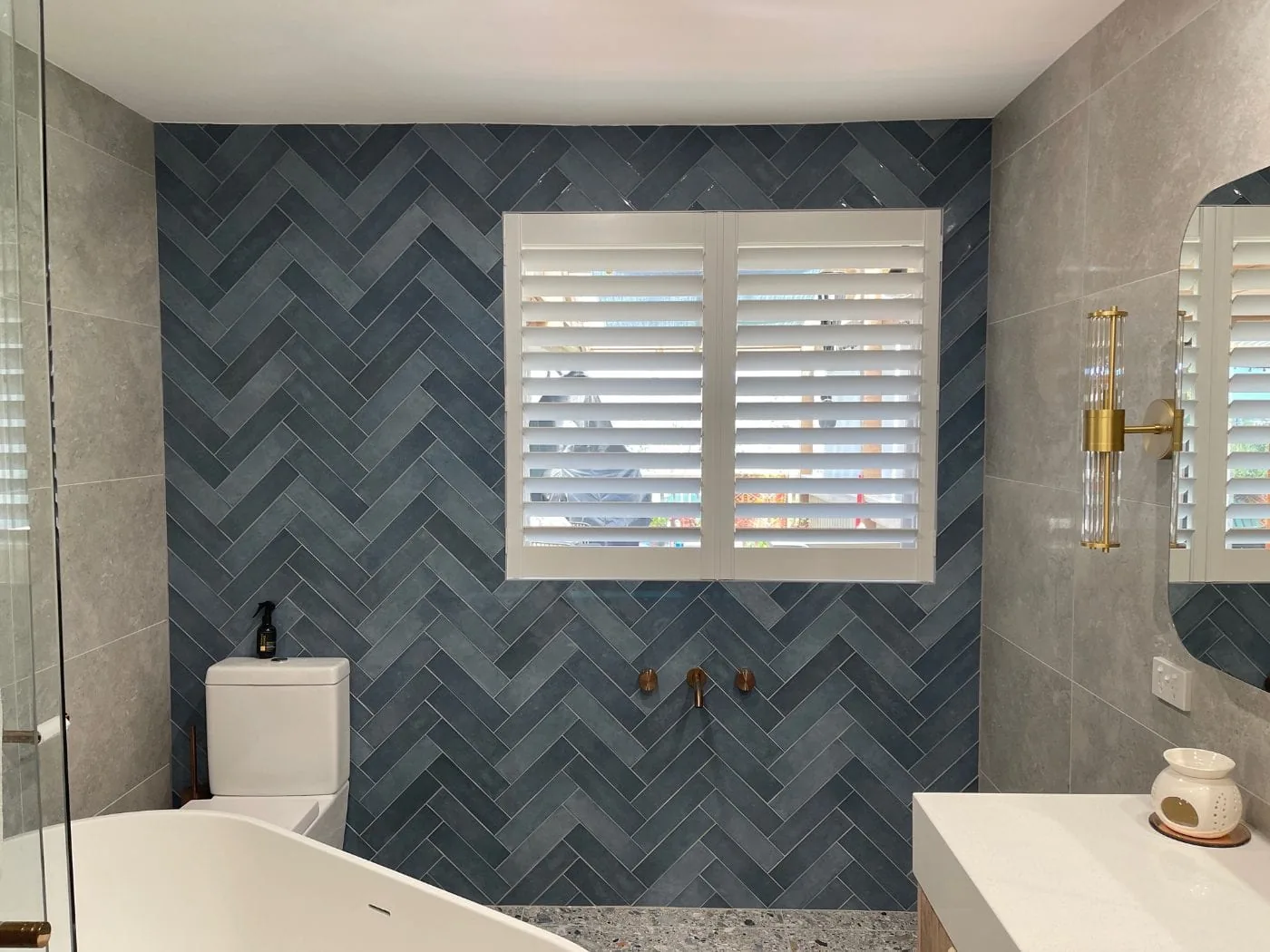 White PVC plantation shutters in a styled bathroom with herringbone tiles and brass fixtures — We Inspire Blinds Melbourne